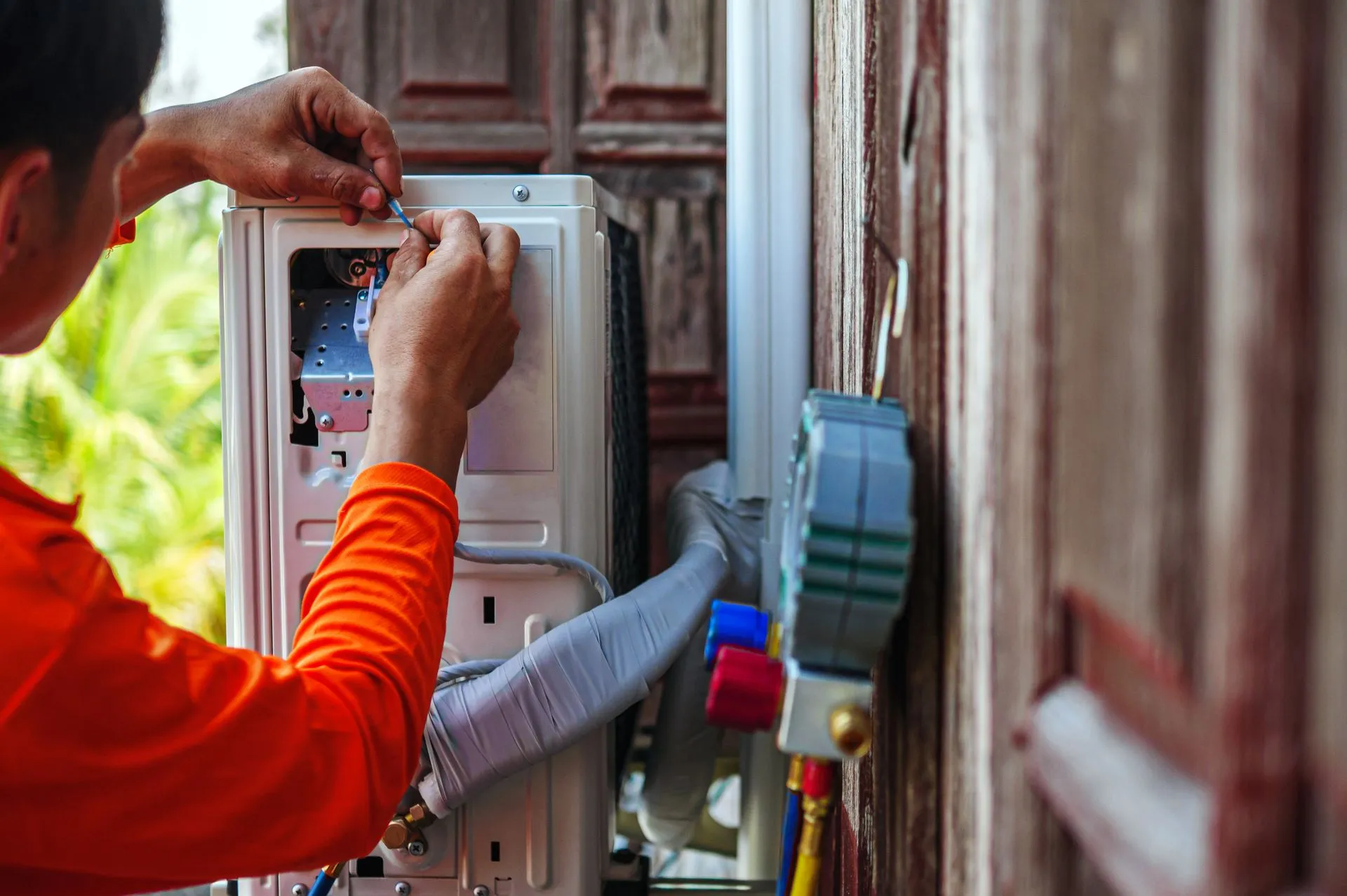 A technician in orange shirt is installing an air conditioner outside.