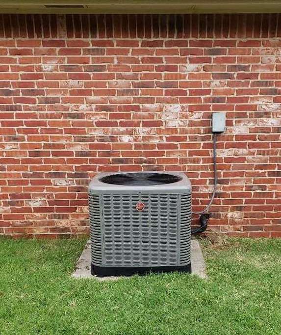 An air conditioner is sitting in the grass in front of a brick wall. An air conditioner is sitting in the grass in front of a brick wall.