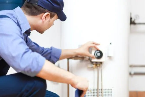 Plumber in blue shirt and cap adjusting a water heater.
