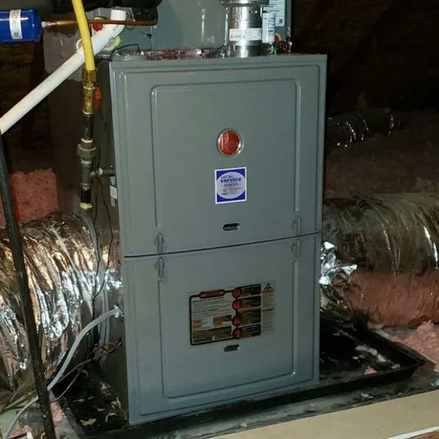 Gray furnace unit in an attic with ductwork and insulation.