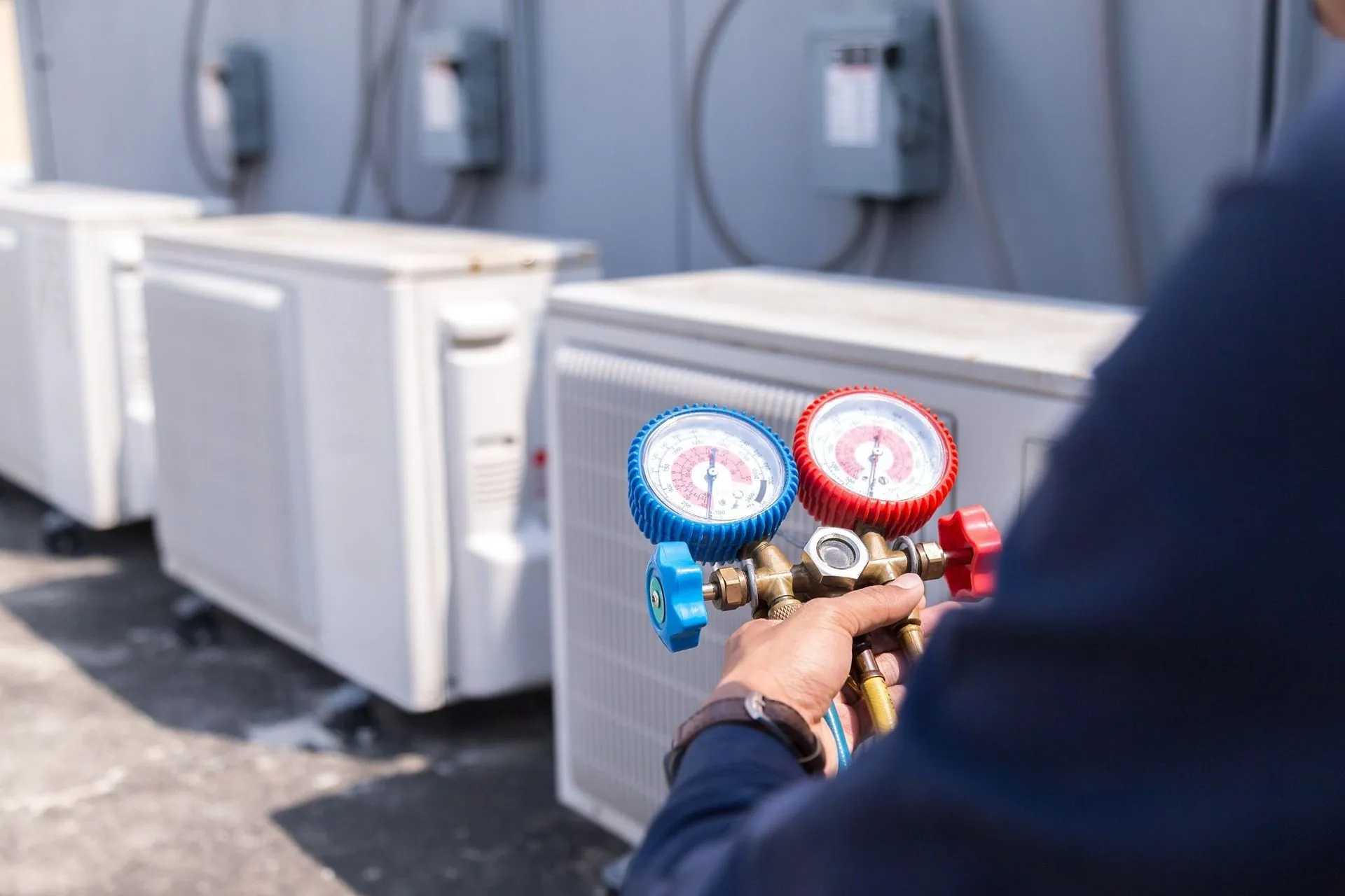 HVAC technician checks air conditioning unit's pressure with gauges. Outdoors, sunlight.