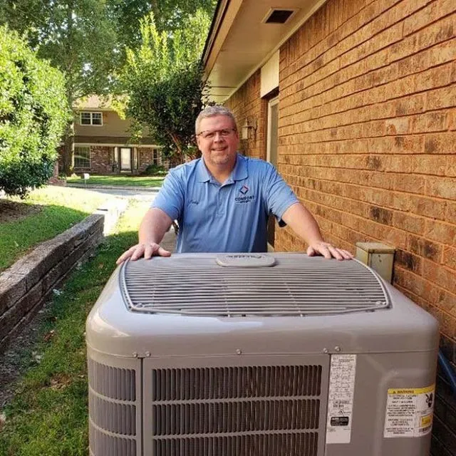 Cody is standing next to a large air conditioner outside of a brick building.